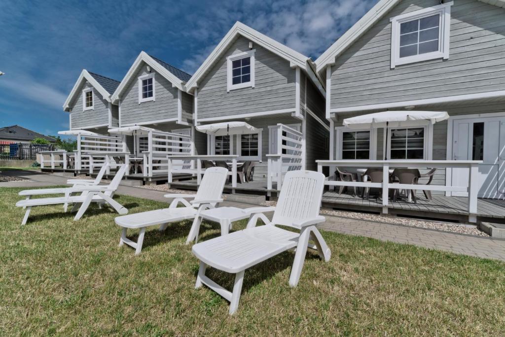 a group of white chairs sitting in the grass in front of a house at Domki letniskowe Kajuta in Władysławowo