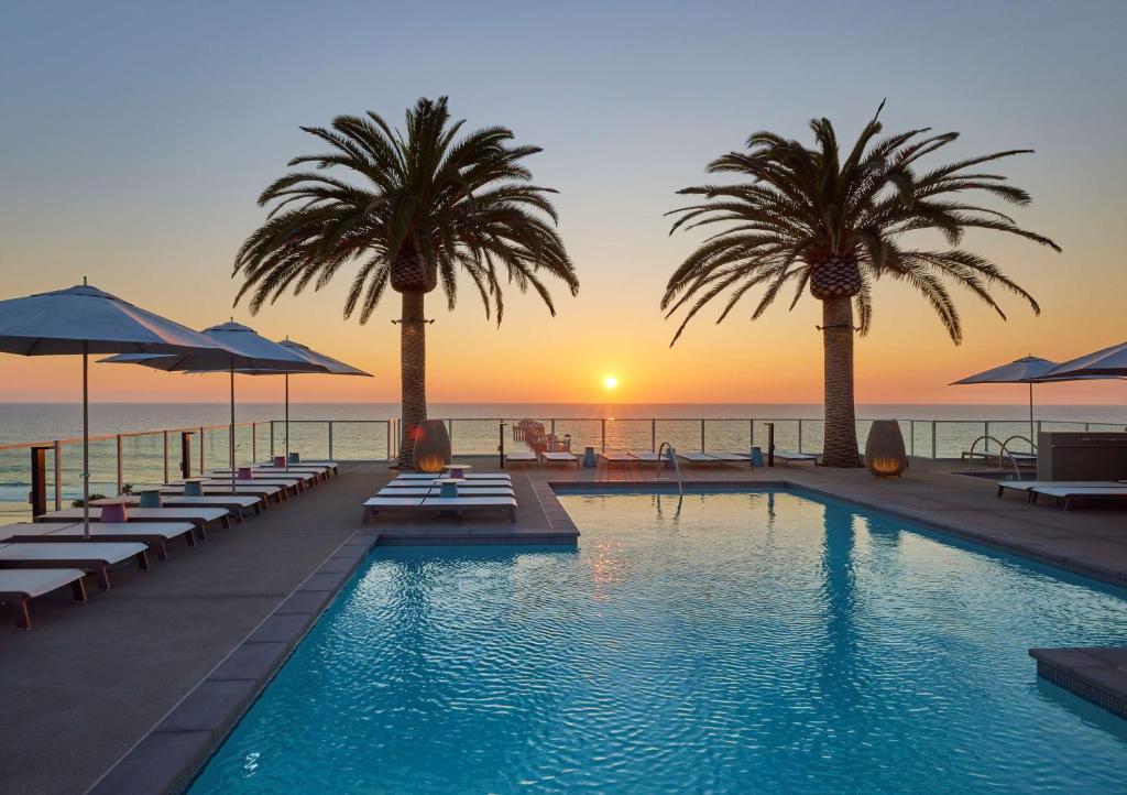 a swimming pool with palm trees and a sunset at Mission Pacific Hotel, part of JdV by Hyatt in Oceanside