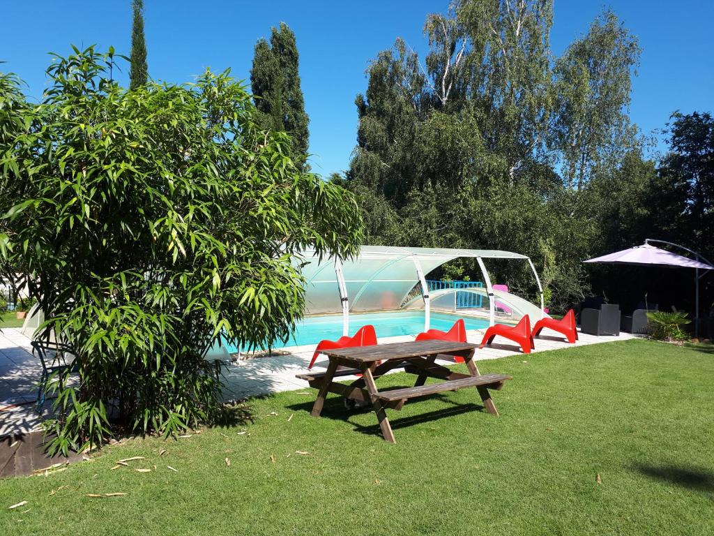 a picnic table and red chairs next to a pool at Chambre D'hôte De La Rotterie in Saint-Mars-dʼOutillé