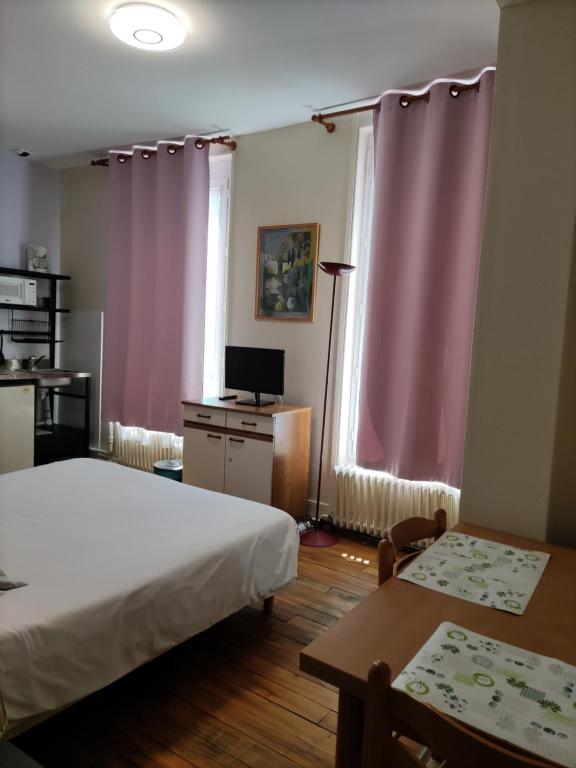 a bedroom with two beds and pink curtains and a table at Le Nid - Studios in Chartres