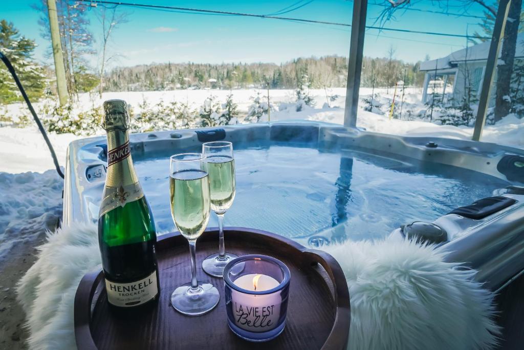 Una botella de champán y dos copas sobre una mesa junto a un jacuzzi. en Chalet Le Convivial Tremblant, en Lac-Supérieur