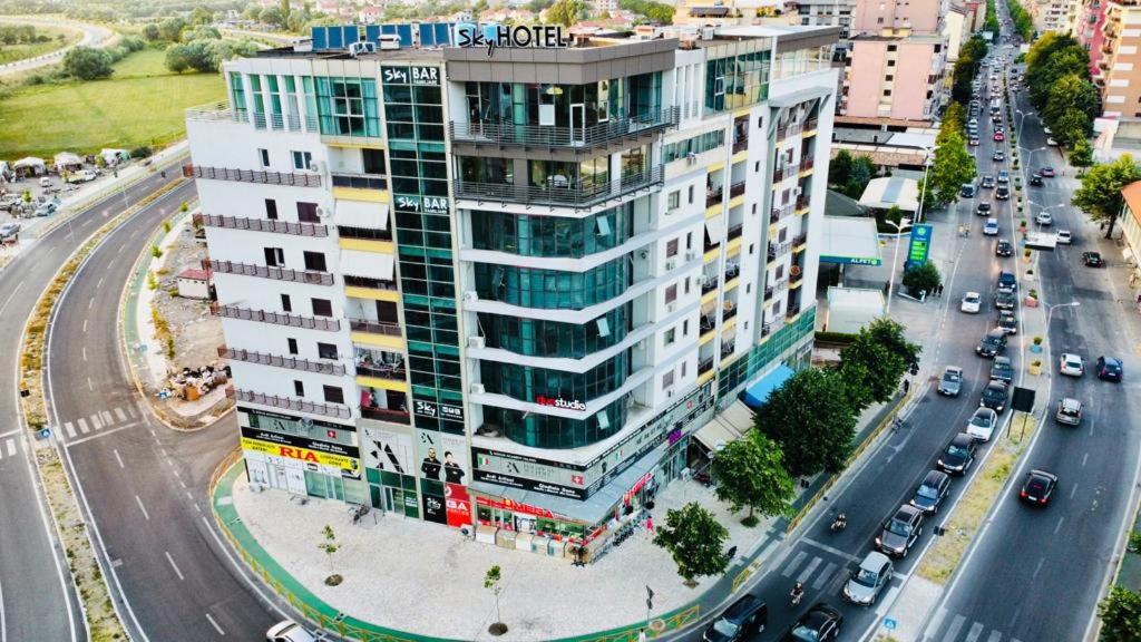 un edificio blanco alto en una calle de la ciudad con coches en Sky Hotel, en Shkodër