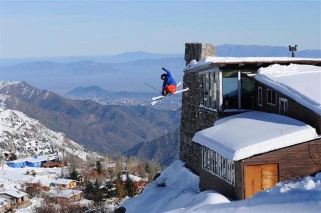 een persoon op ski's die in de sneeuw van een gebouw springt bij Cordillera Hostel in Farellones