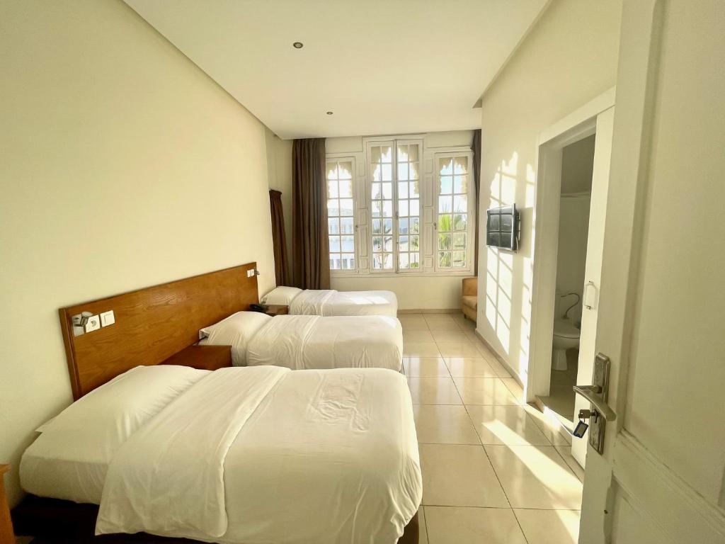 una camera d'albergo con tre letti e una televisione di Hotel Lutece a Rabat