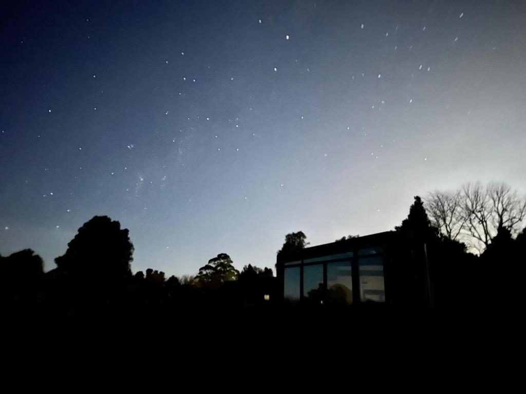 uma casa de vidro no meio de um campo à noite em Ngā Whare Mānatu em Geraldine