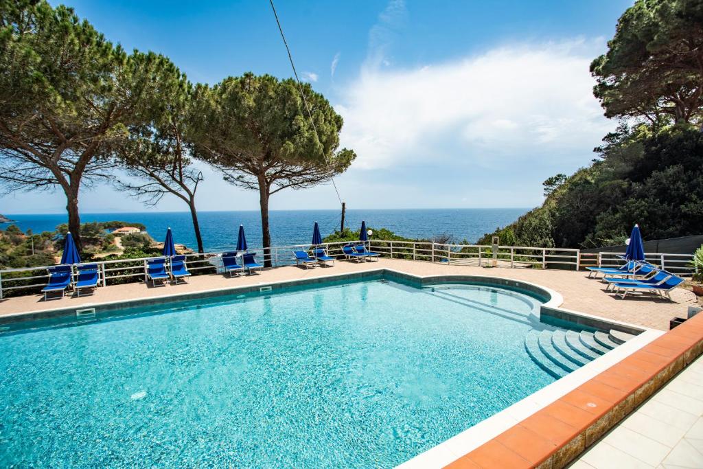 a swimming pool with chairs and the ocean in the background at Residence Reale in Porto Azzurro