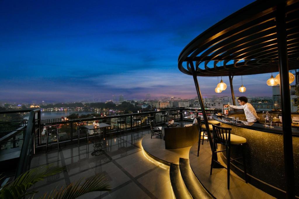 a person sitting at a bar on a balcony at night at Lucien Hanoi Lakeside Hotel & Rooftop in Hanoi