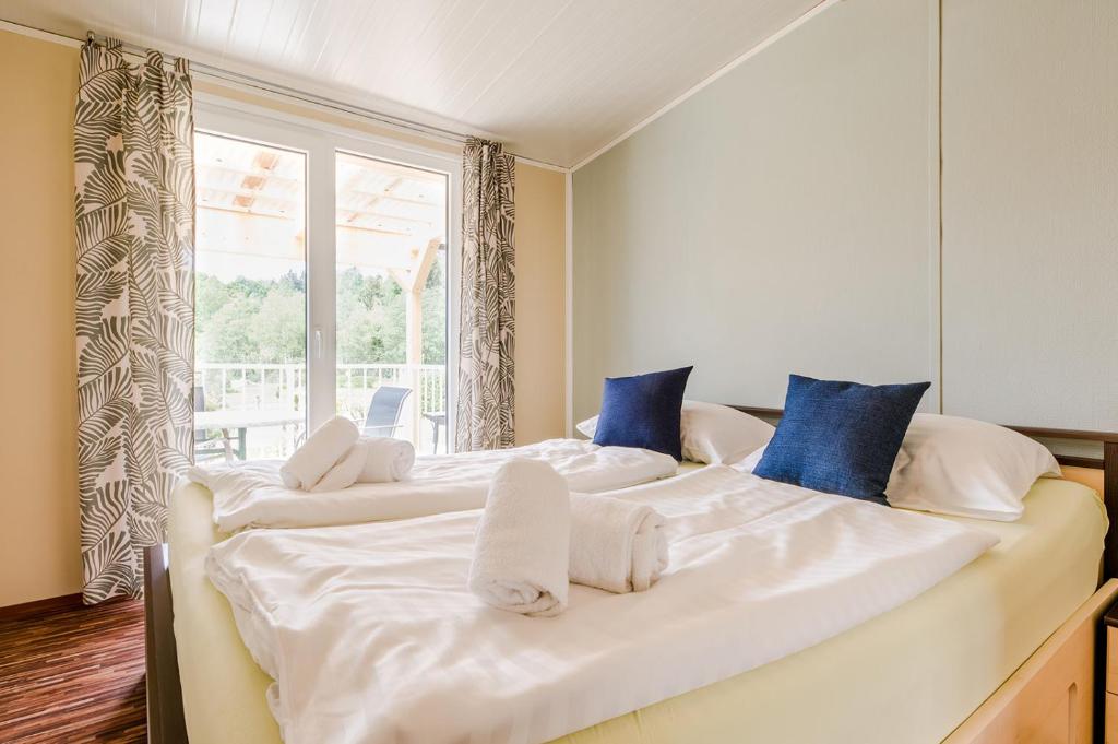 a large bed with white sheets and blue pillows at Relax Camping Seewirt in Feldkirchen in Kärnten