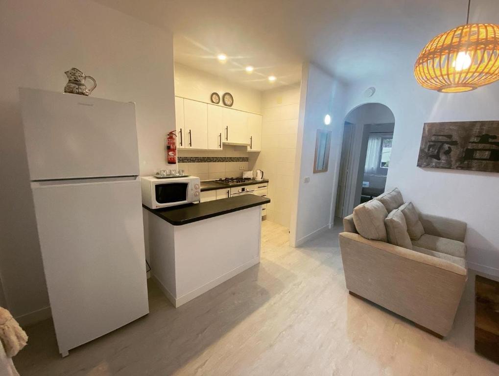 a kitchen with a white refrigerator and a couch at APARTAMENTO CON ENCANTO EN RESIDENCIAL CON PISCINA in Cala'n Porter