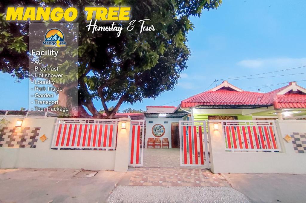 a house with red and white gates and a tree at Mango Tree Homestay & Ijen Tour in Banyuwangi