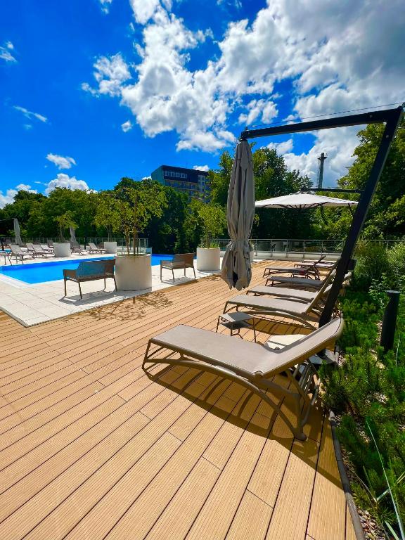 a deck with chairs and an umbrella and a pool at Apartament Nadmorski Hampton in Kołobrzeg
