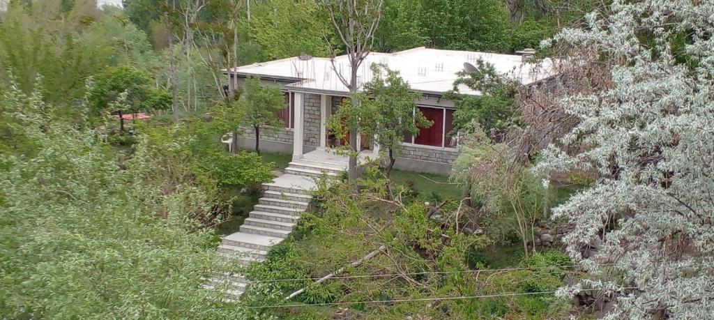 a white house with a red door in a forest at Fort and Indus River View Guest House in Skardu