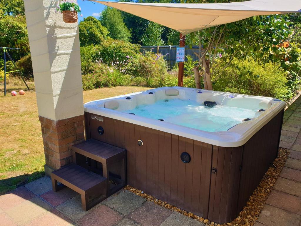 une baignoire jacuzzi assise sous un parasol et un tabouret dans l'établissement Lions Lodge: Great location with hot tub, à Ringwood