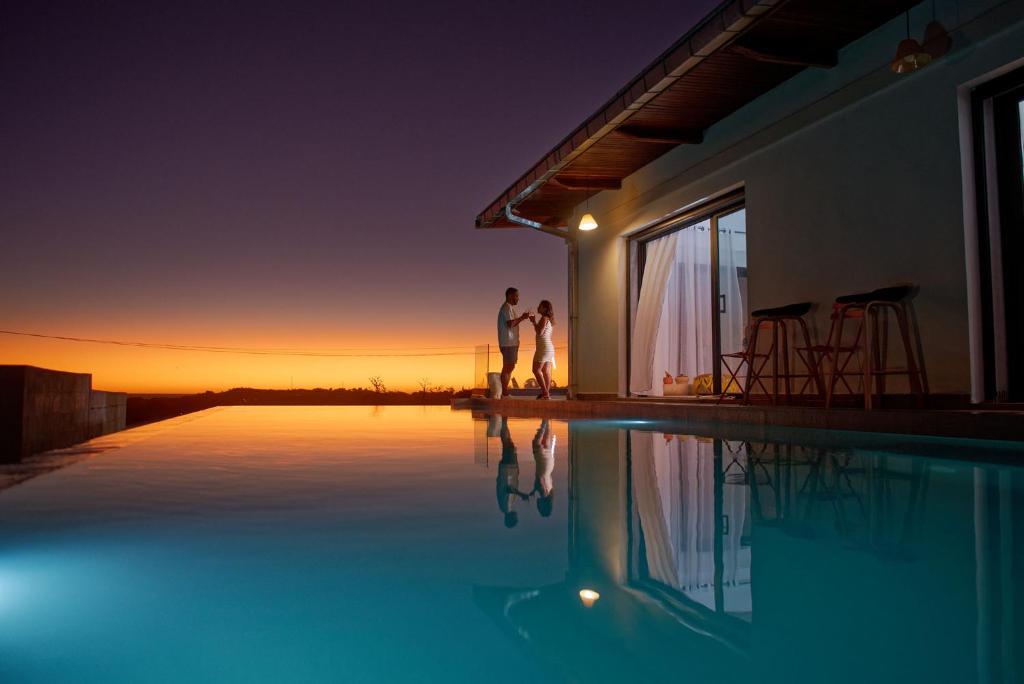 a couple standing next to a swimming pool at sunset at Villa Vintana Nosy Be in Nosy Be