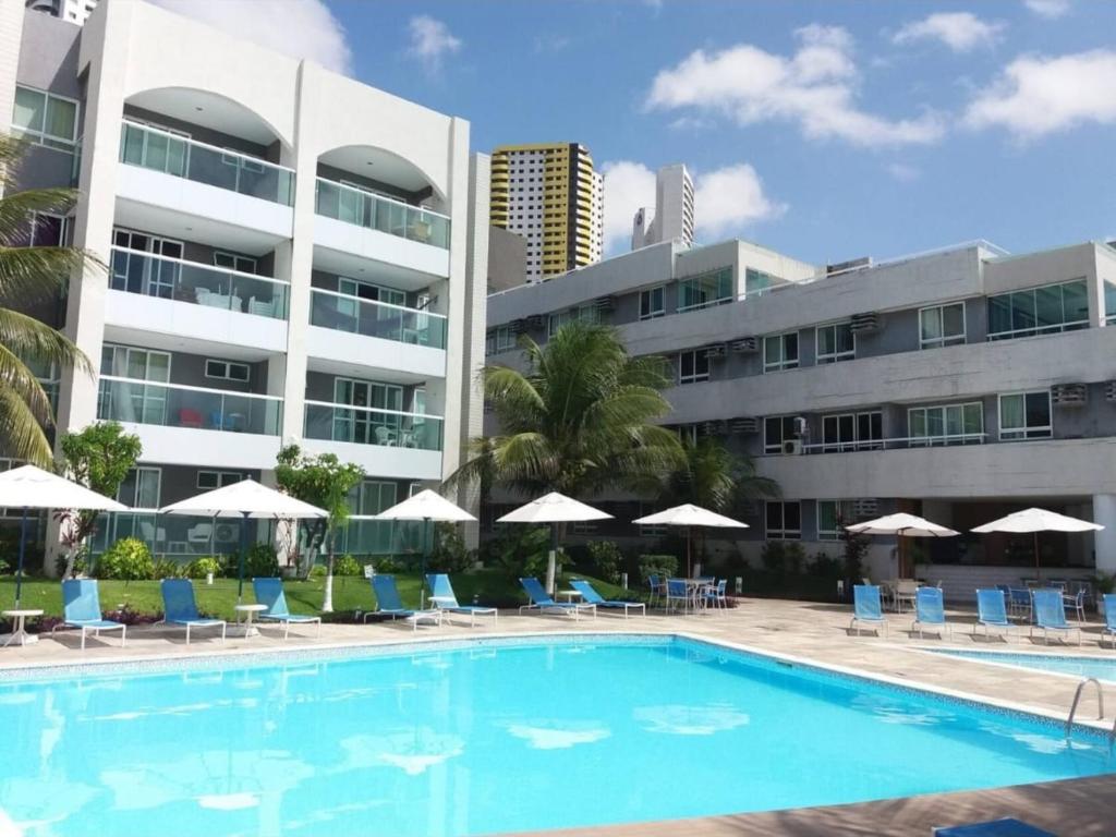 a swimming pool with chairs and umbrellas in front of a building at FLAT PONTA NEGRA BEACH-Natal in Natal