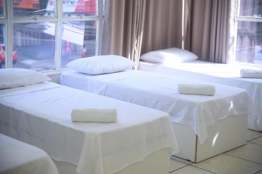 three beds with white linens in a room with a window at Hotel Jurubatuba in São Bernardo do Campo