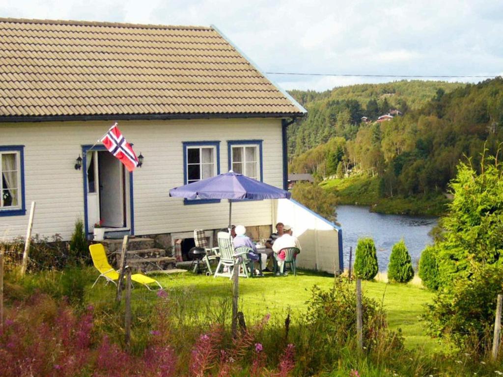 dos personas sentadas bajo un paraguas en el patio de una casa en 6 person holiday home in lyngdal, en Lyngdal