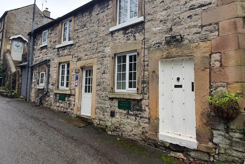 ein altes Steingebäude mit weißen Türen auf einer Straße in der Unterkunft Anne Cottage, Bakewell, in the Peak District in Bakewell