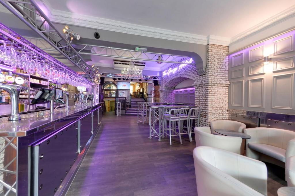 un bar con iluminación púrpura, mesas y sillas en The George Hotel, en Whitby