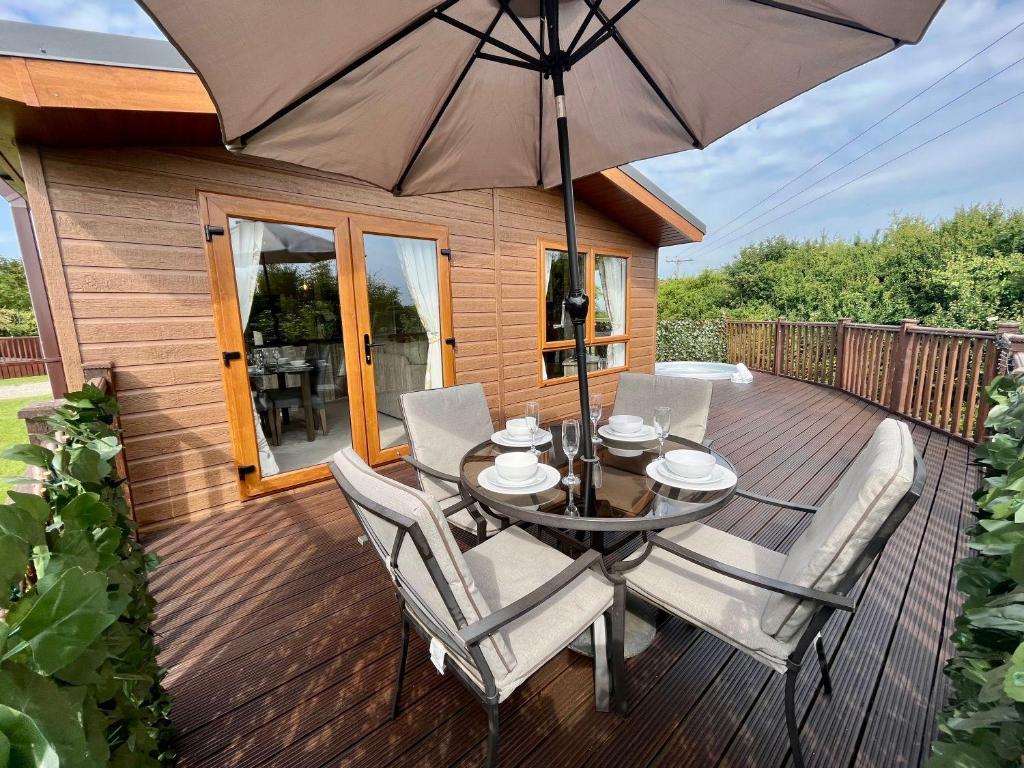a wooden deck with a table and chairs and an umbrella at Buttercup Lodge With Hot Tub in Little Habton