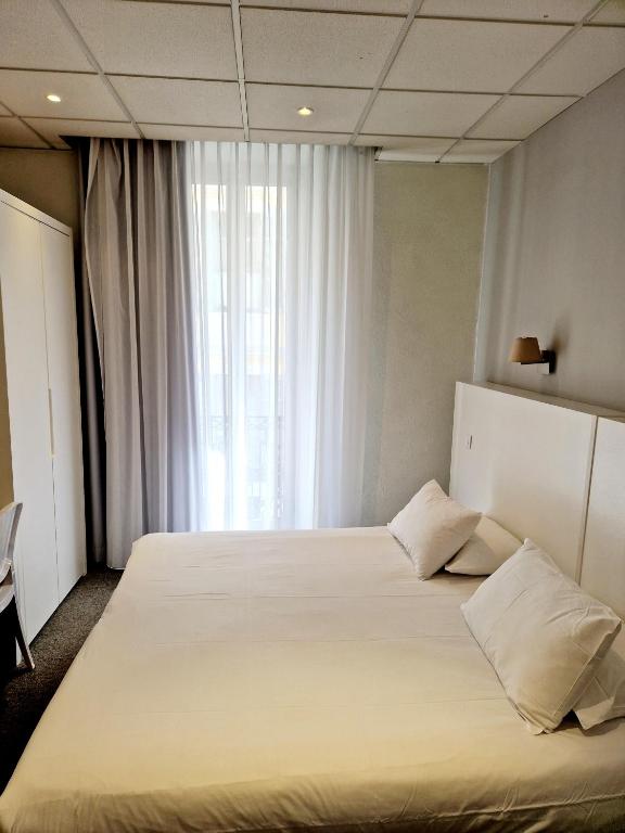 a bedroom with a large white bed with a window at Hôtel P.L.M. in Cannes