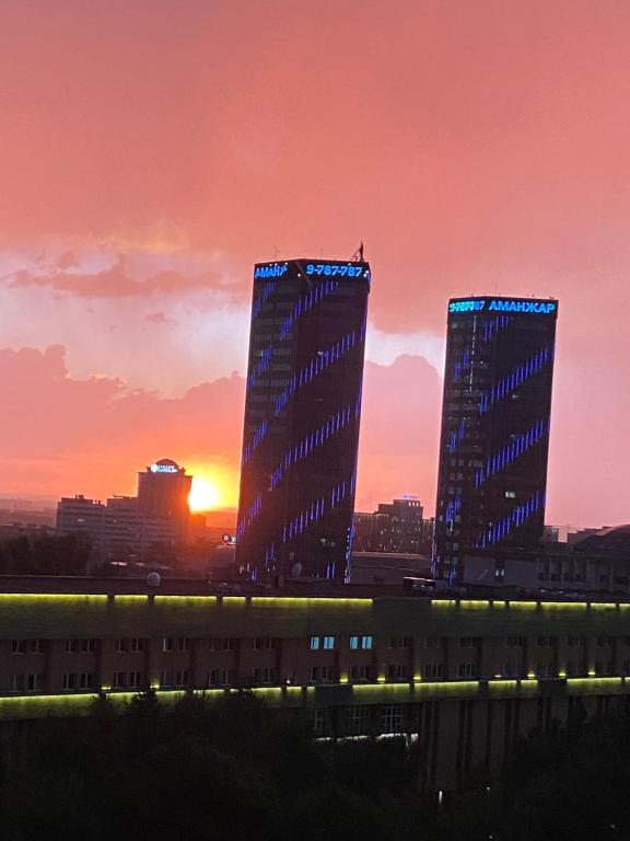 dois edifícios altos em uma cidade ao pôr do sol em Квартира в центре Алматы em Almaty