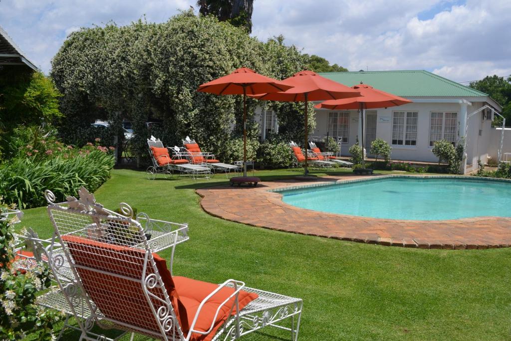 a yard with a swimming pool with chairs and umbrellas at A Tapestry Garden Guest House in Potchefstroom