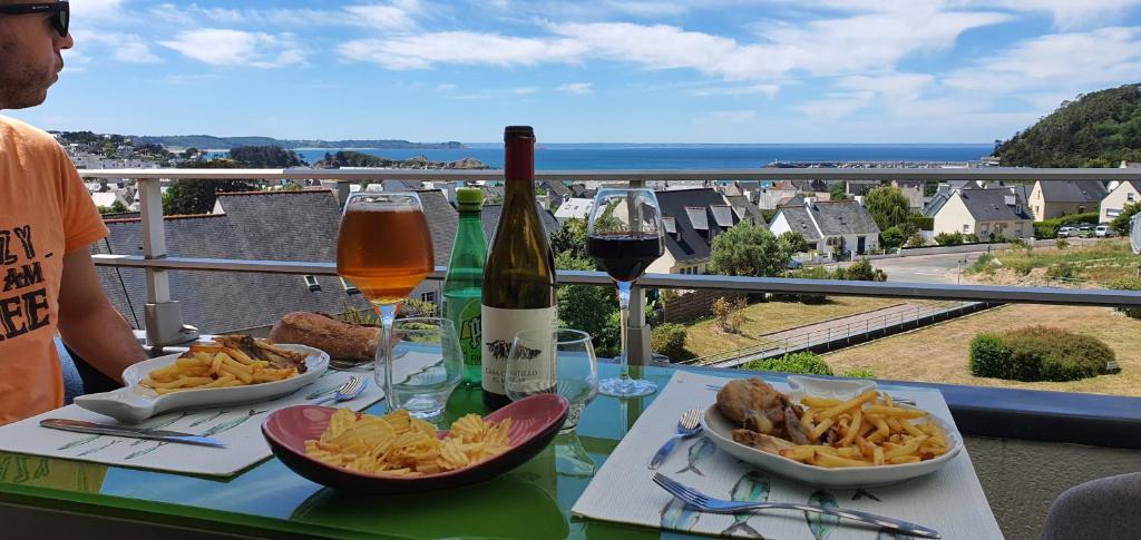 een man aan een tafel met eten en een fles wijn bij Appartement Bretagne vue mer exceptionnelle sur les hauts d'Erquy au calme ! et au pied du GR34 in Erquy