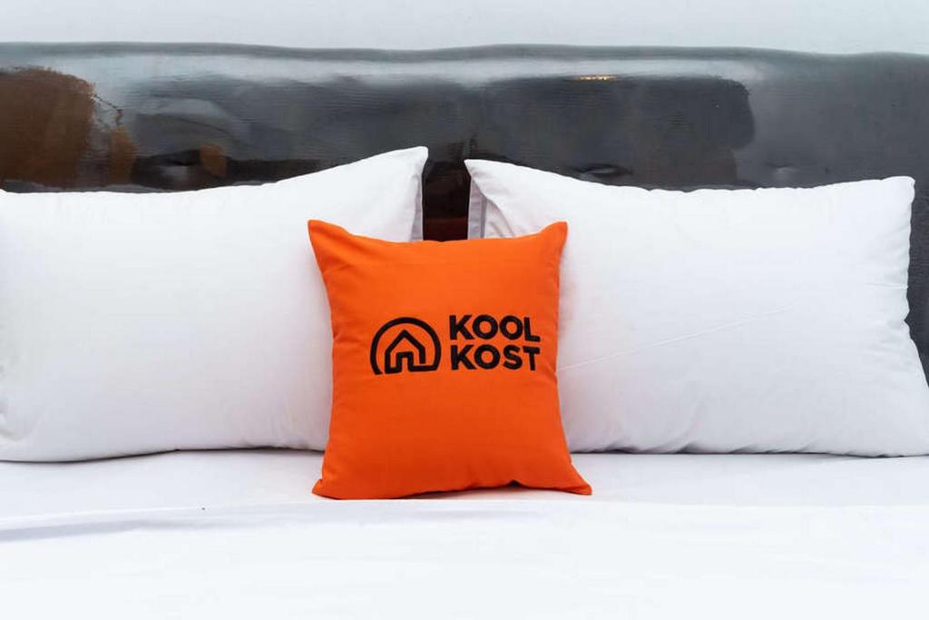 an orange pillow sitting on a bed with four white pillows at KoolKost near Fakultas Teknik UGM Male Only - Minimum Stay 6 Nights in Kejayan