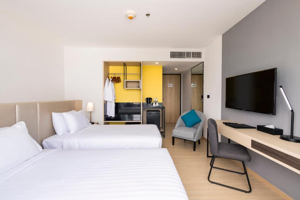 A two-bed room with a long desk, television, lounge chair and open storage area.