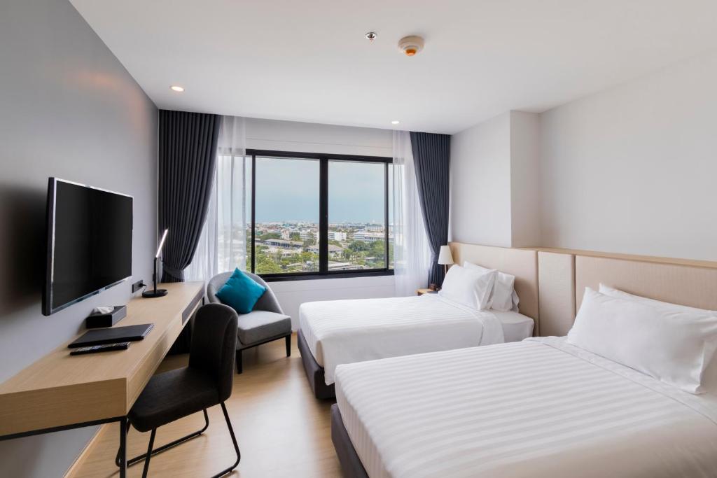 A twin room with two beds, a television, desk, armchair, and city-facing window.
