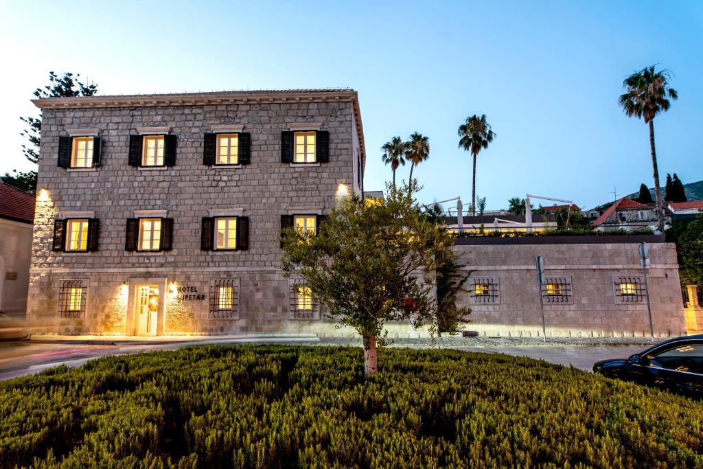 un gran edificio de ladrillo con un árbol delante de él en Hotel Supetar en Cavtat