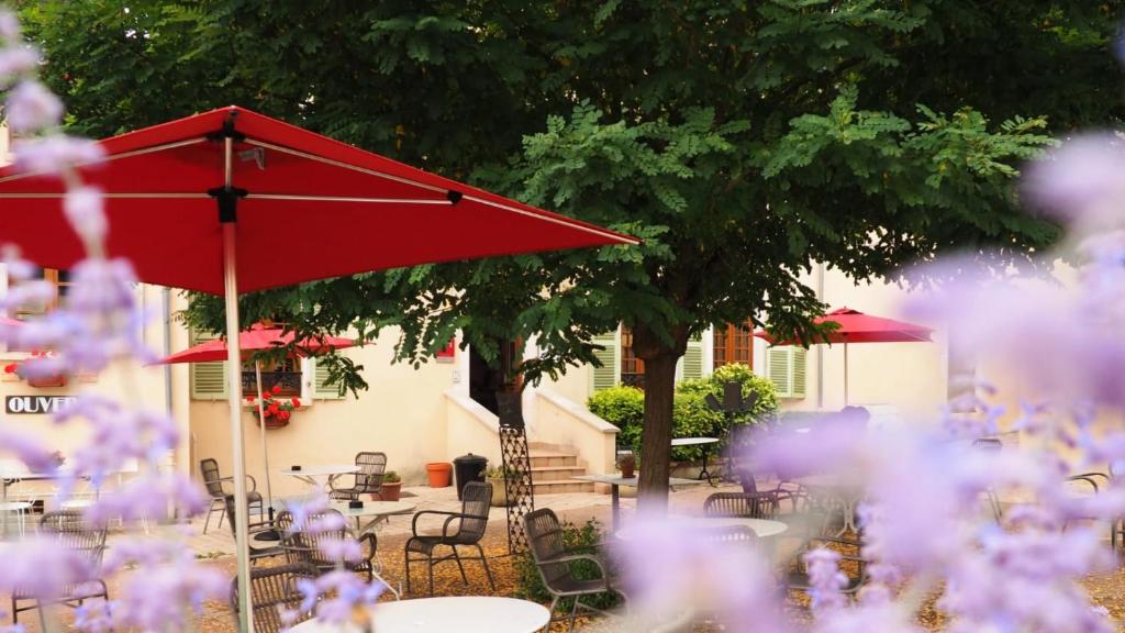 un parasol rouge, des tables, des chaises et des fleurs violettes dans l'établissement Hostellerie du Chateau Bellenaves, à Bellenaves