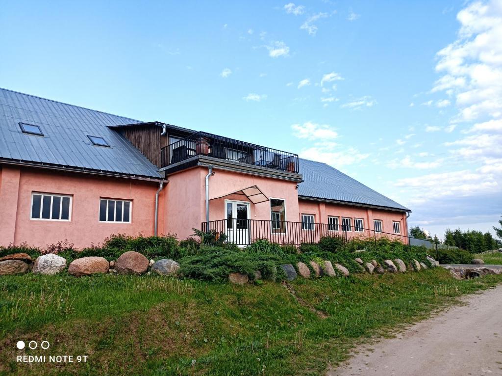 ein rosa Haus mit schwarzem Dach auf einer unbefestigten Straße in der Unterkunft Lapegles 2 in Ludza