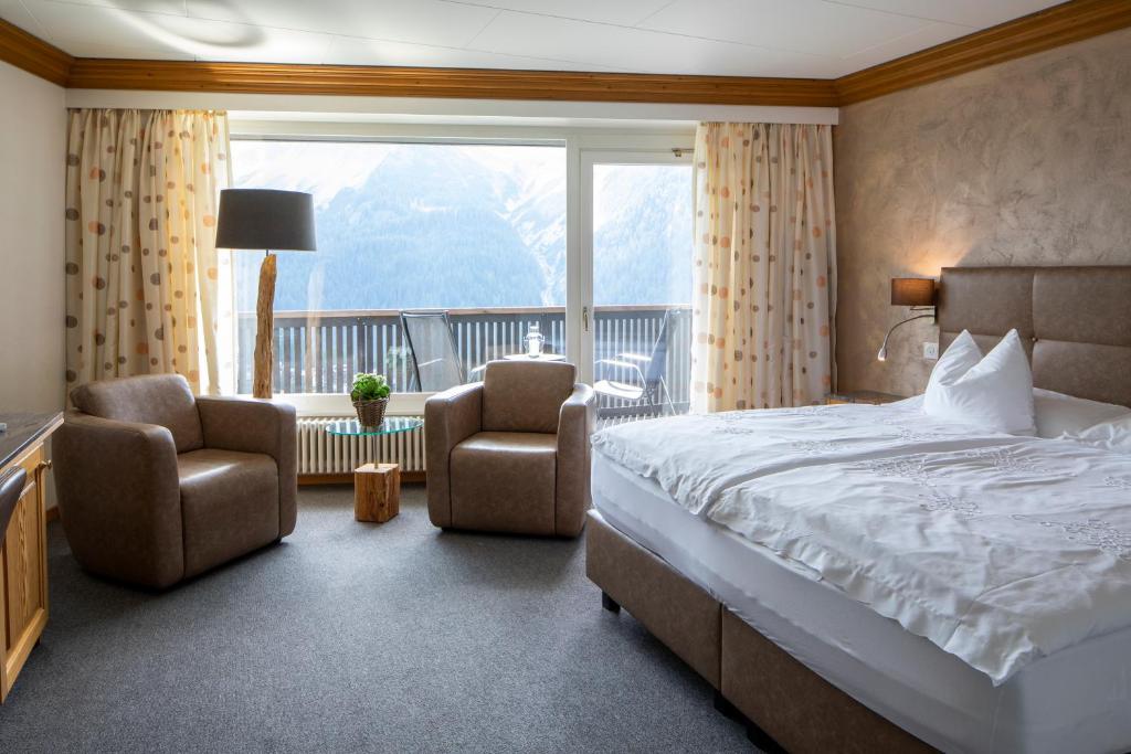 ein Schlafzimmer mit einem Bett, 2 Stühlen und einem großen Fenster in der Unterkunft Cristallo Arosa Hotel in Arosa