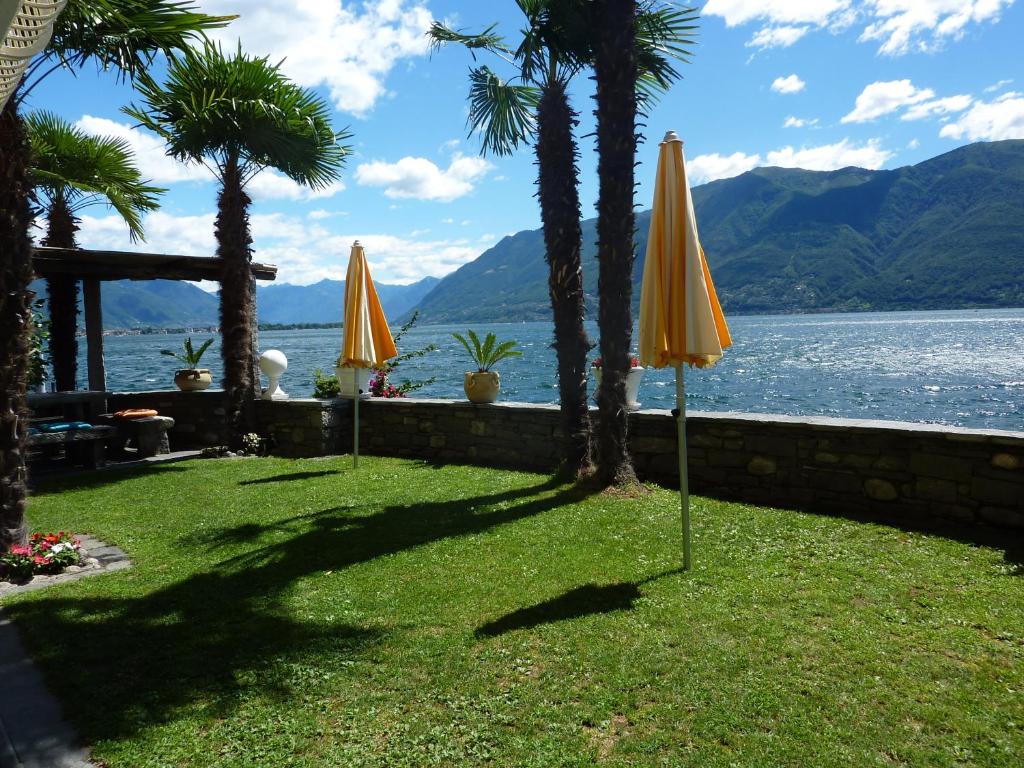 龍科索普拉阿斯科納的住宿－Casa Conti al Lago，两把黄伞坐在水边的草地上