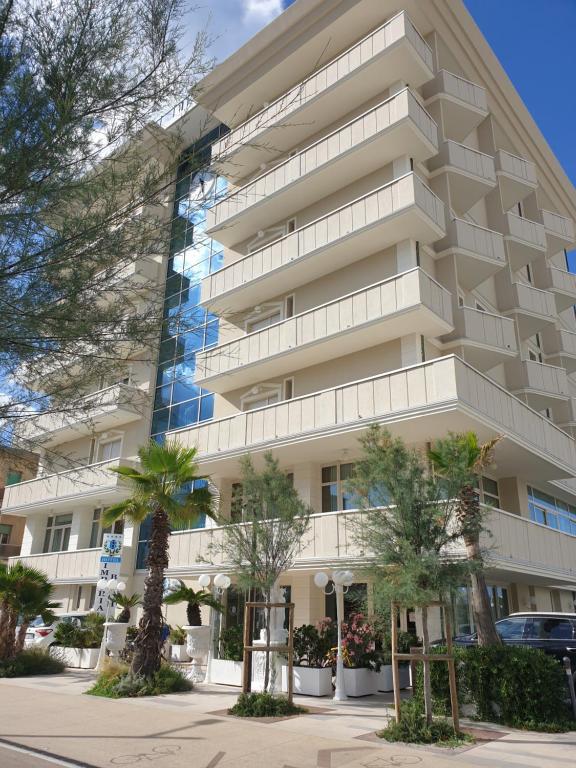 a tall white building with palm trees in front of it at Hotel Imperial Beach - Dada Hotels in Rimini