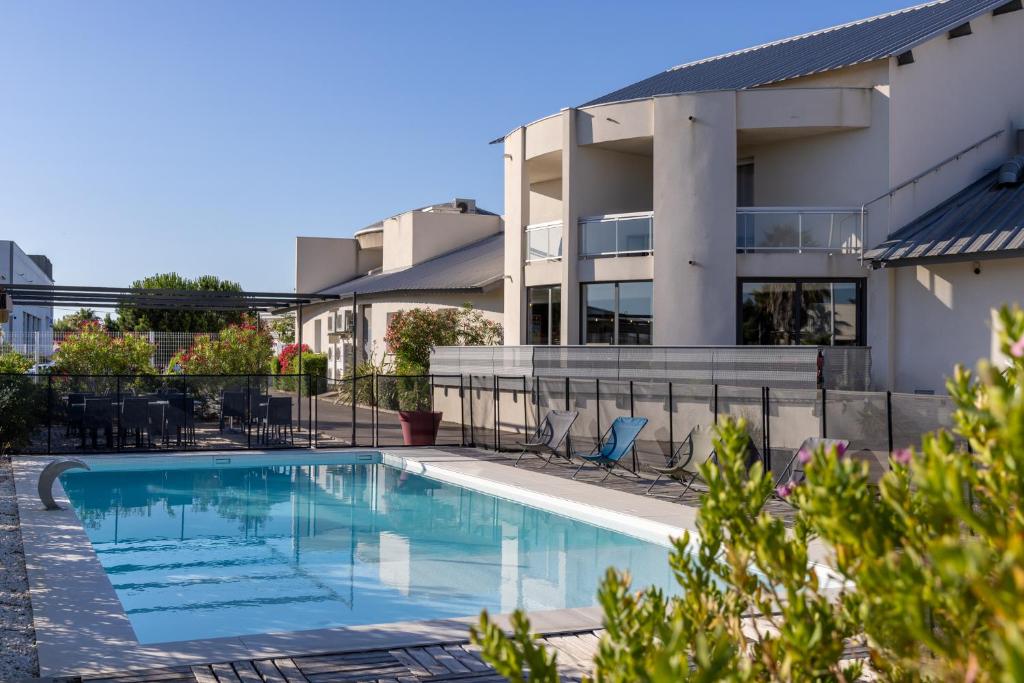 a swimming pool in front of a building at The Originals City, Hôtel Les Dômes, Perpignan Sud Saleilles in Perpignan