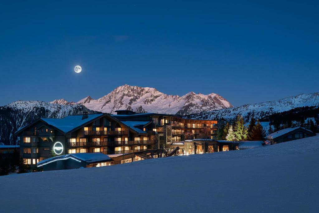 ein großes Gebäude im Schnee bei Nacht mit dem Mond in der Unterkunft Hotel Annapurna in Courchevel