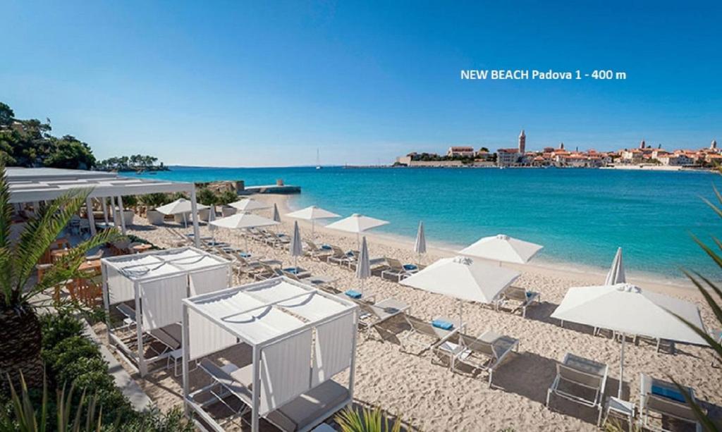 a beach with white umbrellas and chairs and the ocean at Evergreen & Pinky Apartments close to the Beach in Rab