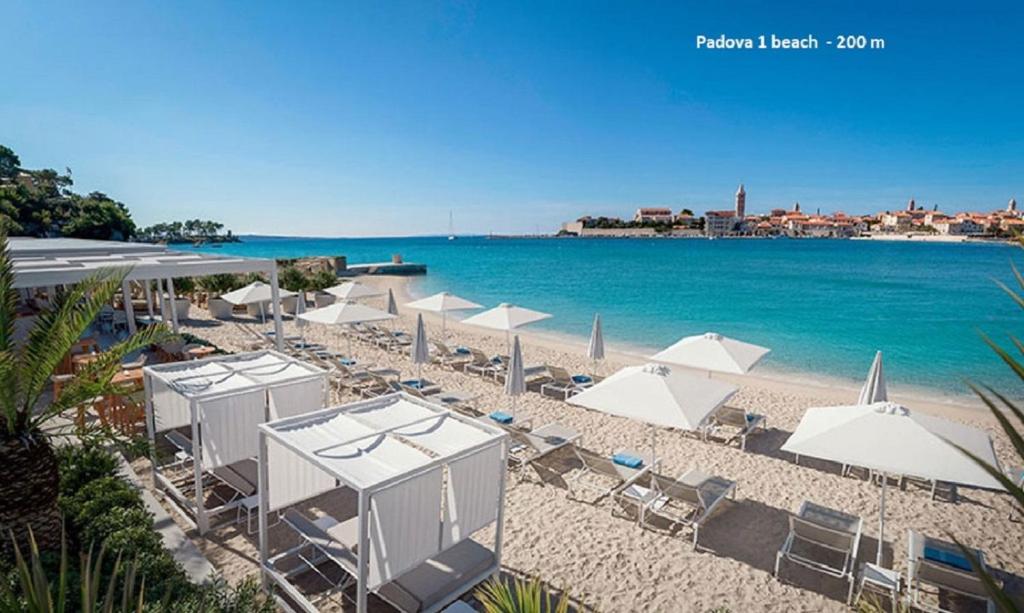 a beach with white umbrellas and chairs and the ocean at MiraMar Gardenn Apartmment in Rab