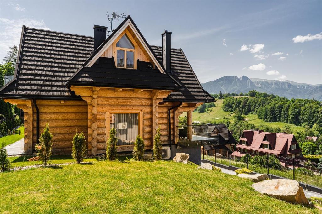 a log cabin with a black roof on a green lawn at Osada Bachledzki Wierch Odkryj Zakopane in Zakopane