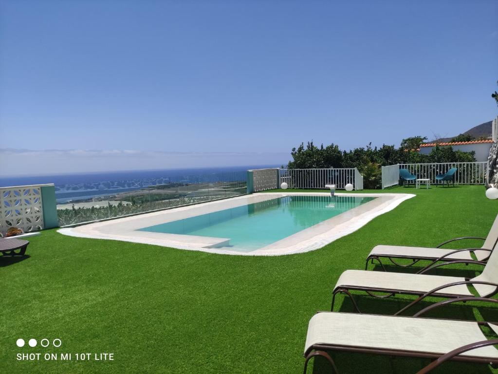 una piscina en un césped con sillas y el océano en Casa Nine con piscina en Breña Baja
