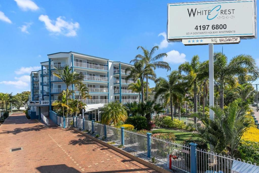 a sign in front of a building with palm trees at White Crest Apartments in Hervey Bay