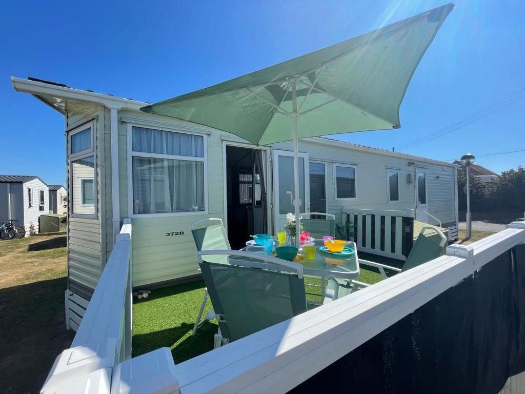 a patio with a table and a green umbrella at 27 Tower View Pevensey Bay Holiday Park in Pevensey