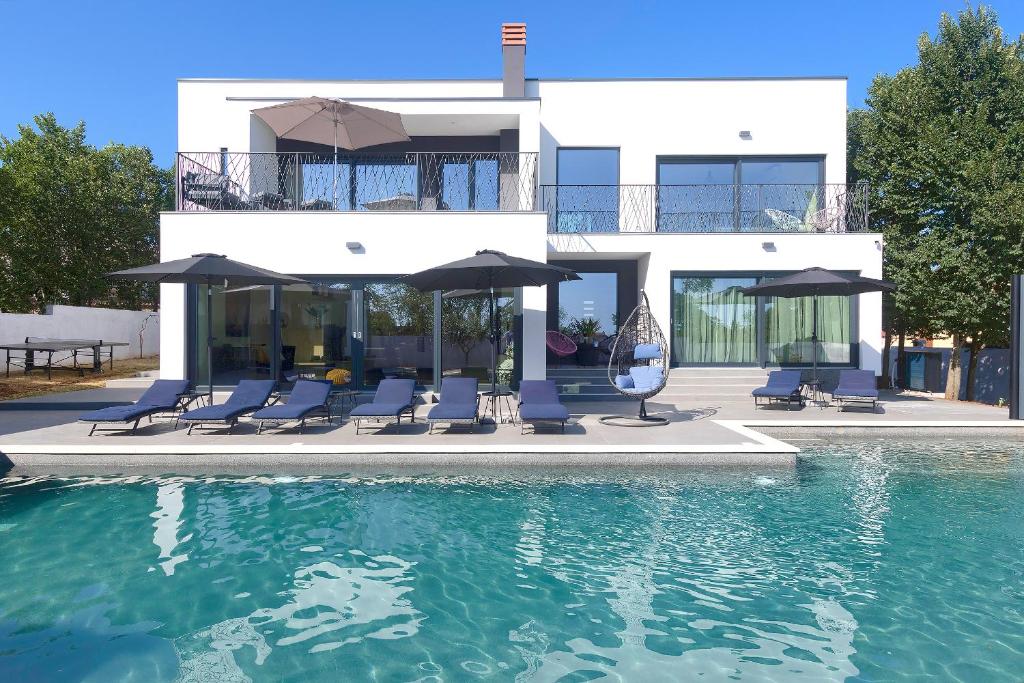 a house with chairs and umbrellas next to a swimming pool at Villa Valdo by Istra Vacation in Marčana