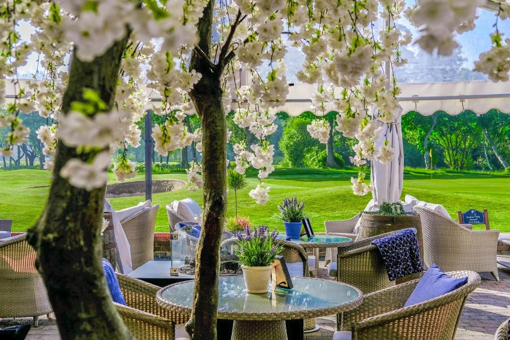 a patio with tables and chairs and trees with flowers at Formby Hall Golf Resort & Spa in Southport