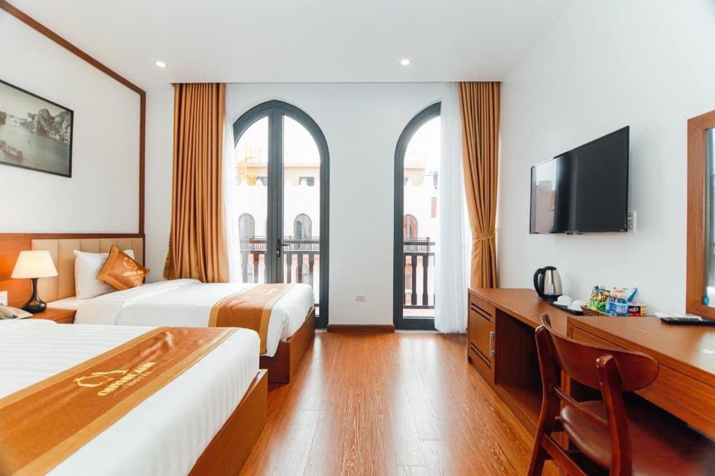 a hotel room with two beds and a desk and a tv at Quỳnh Anh Hotel Hạ Long in Ha Long