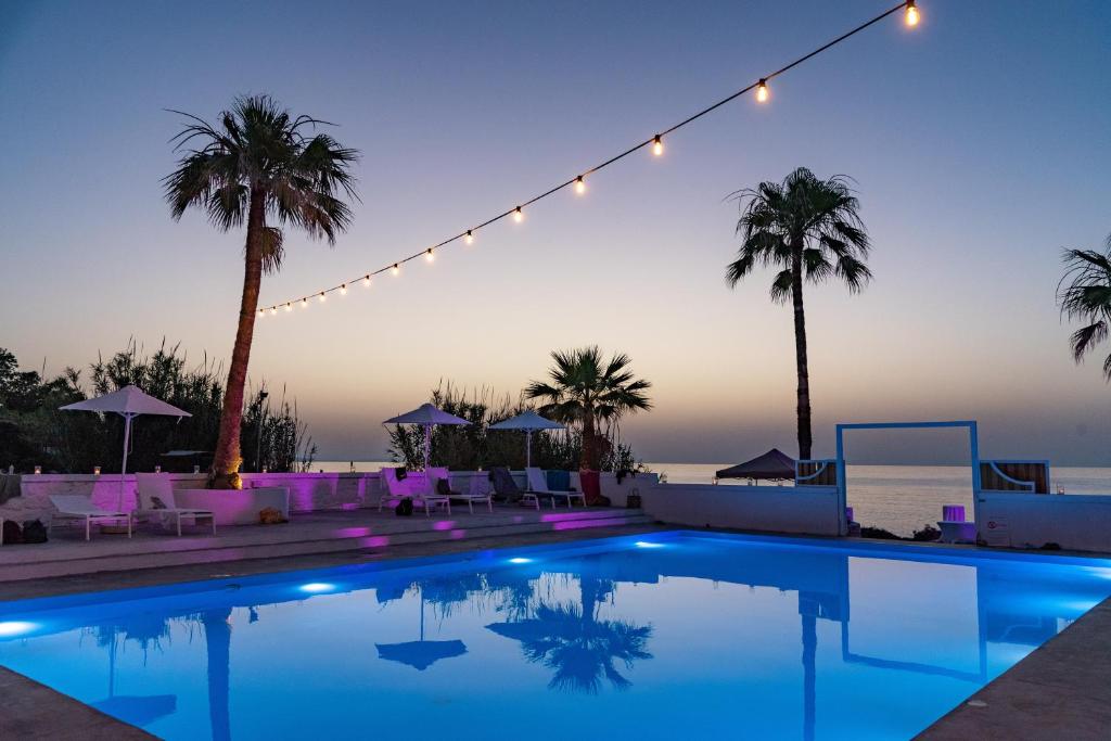 a swimming pool at night with palm trees and lights at Thalasses in Adelianos Kampos