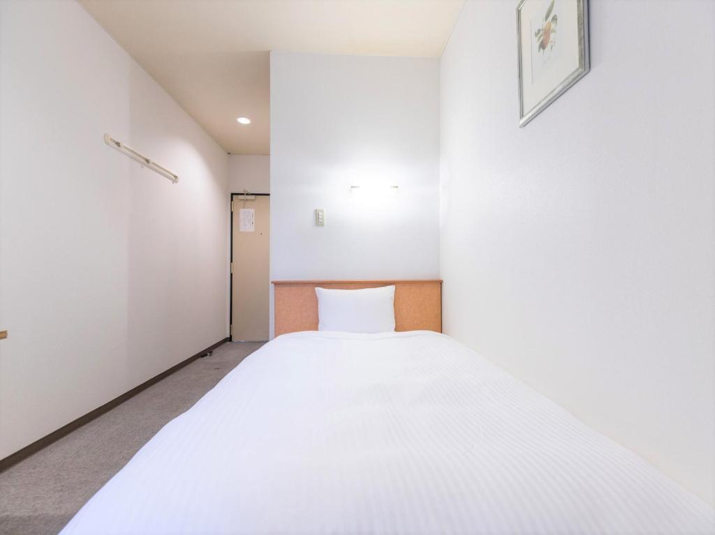 Habitación blanca pequeña con cama. en Hotel Isesaki East en Isesaki